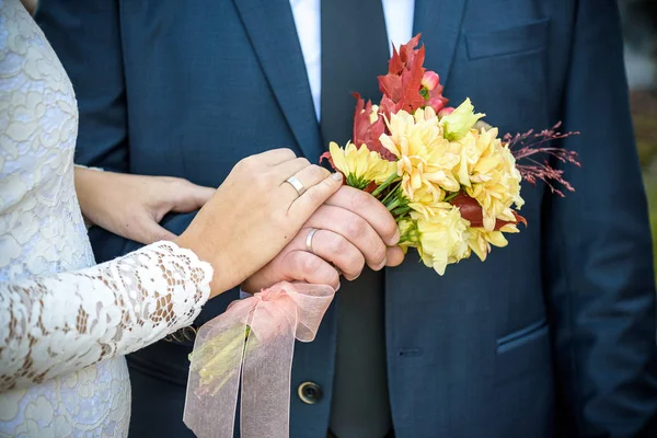 特写镜头。新娘和新郎的手。新娘和新郎握住手。把重点放在圆环上。手中的花束 — 图库照片