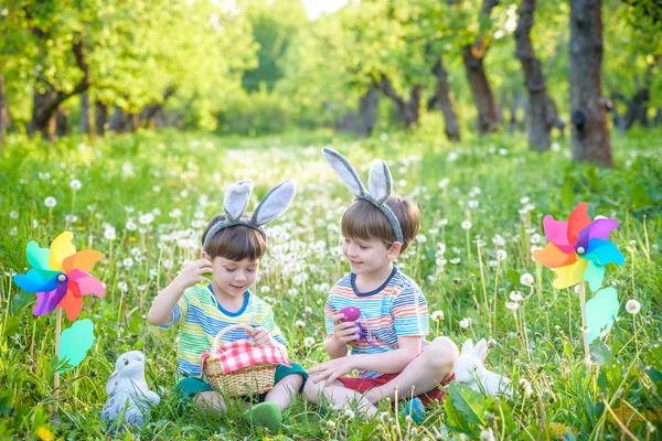 Дети веселятся и играют с пасхальными яйцами. Два веселых мальчика сидят на лужайке после охоты за пасхальными яйцами — стоковое фото