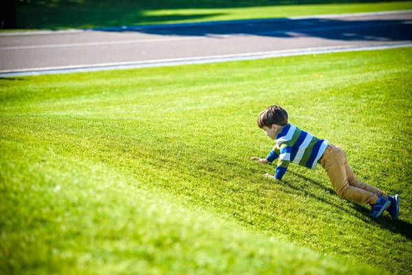 Caucasian boy climbs up on fresh green grass meadow, happy kids — Stock Photo, Image