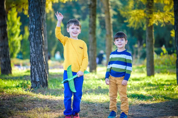 Szczęśliwa dwójka braci bawiących się zabawkowym samolotem na tle błękitnego letniego nieba. Chłopcy wrzucają piankowy samolot do lasu lub parku. Najlepsza koncepcja dzieciństwa — Zdjęcie stockowe