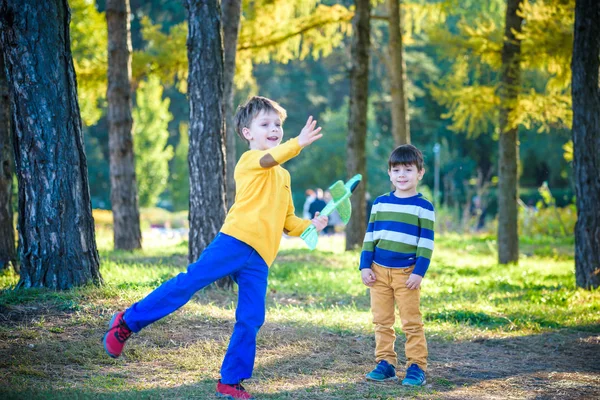 Happy two brother kids playing with toy airplane against blue summer sky background. Boys throw foam plane in the forest or park. Best childhood concept — Stock Photo, Image