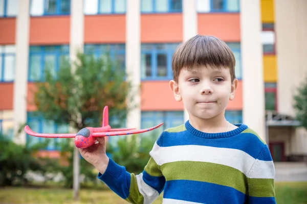 Mutlu bir çocukluk oyuncak uçak hoş binanın arka plan ile oynarken. Çocuk atmak köpük uçak okul veya anaokulu alanındaki. En iyi çocukluk kavramı — Stok fotoğraf