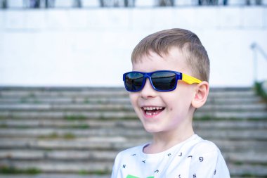 Korkmuş şaşırmış şaşkın karışık beyaz erkek çocuk güneş gözlüklü, pozlar tuğla beyaz duvar arka planı.