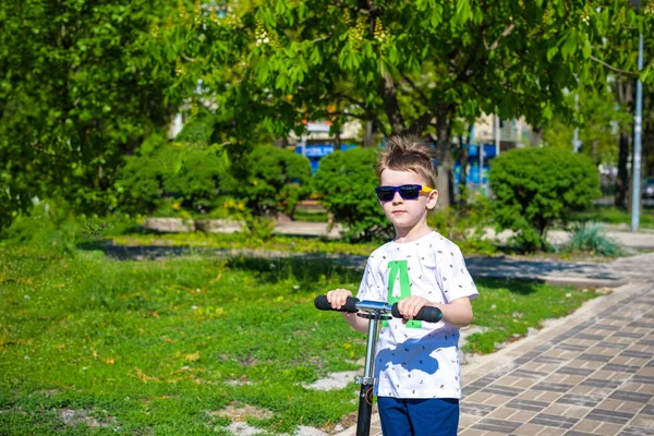 Joyeux petit garçon promenades scooter sur la route dans le parc — Photo