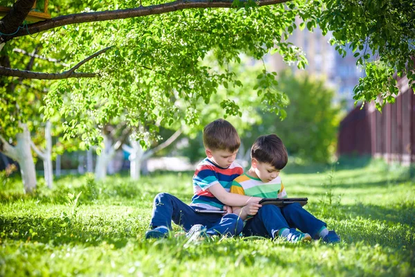 Zwei Geschwisterkinder liegen mit Tablet im Gras. — Stockfoto