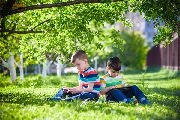 Zwei Geschwisterkinder liegen mit Tablet im Gras. — Stockfoto