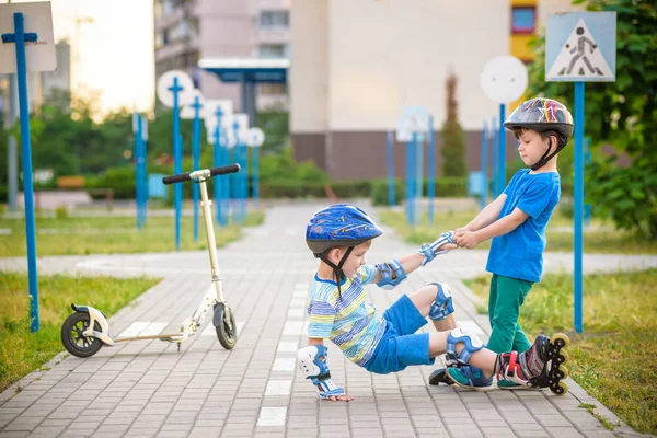 Dos chicos en el parque, ayudar a chico con patines para ponerse de pie —  Fotos de Stock