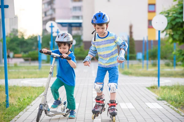 Two kid boy on roller skates and his sibling brother on scooter — Stock Photo, Image