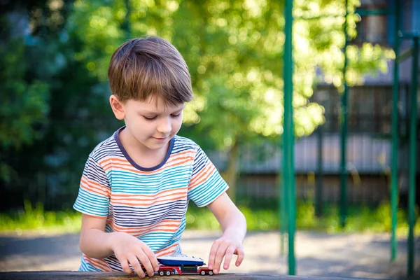 El chico juega con coches de juguete. Un chico jugando solo en el patio. Diversión diurna infantil — Foto de Stock
