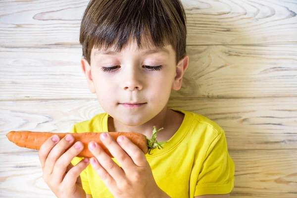 Маленький хлопчик має моркву в руці, дивиться пальцем на — стокове фото