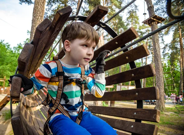 Criança feliz supera obstáculos no parque de aventura corda. Conceito de férias de verão. Menino brincando no parque de aventura corda. Parque de diversões moderno para crianças. Jogos ao ar livre. — Fotografia de Stock