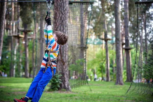 Lächelnder Junge reitet Seilrutsche. Glückliches Kind an der Seilrutsche. das k — Stockfoto