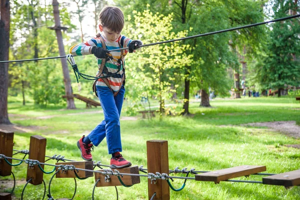 Fröhliches Kind spielt im Abenteuerpark, hält Seile und klettert — Stockfoto