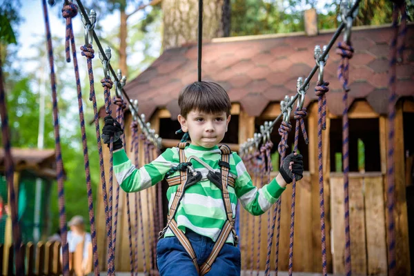 Criança feliz jogando no parque de aventura, segurando cordas e escalada — Fotografia de Stock