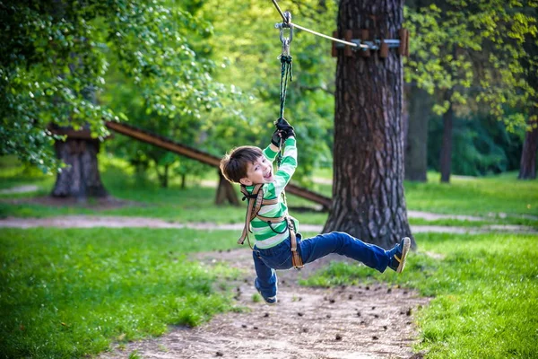 Ragazzo sorridente cavalca una zip line. bambino felice sulla zip line. La k — Foto Stock