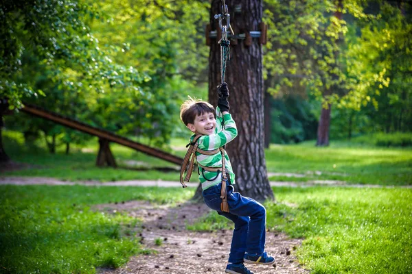 Lächelnder Junge reitet Seilrutsche. Glückliches Kind an der Seilrutsche. das k — Stockfoto