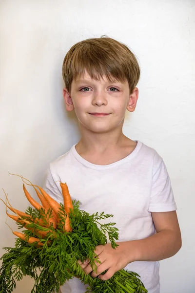 Хлопчик їсть свіжу моркву ізольовано на білому тлі — стокове фото
