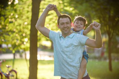 Baba ve oğul sarılma ve birlikte yeşil doğada sıcak güneşli yaz akşam çalıyor. Çocuklar ve ebeveynler, mutlu bir aile arasındaki dostluk kavramı