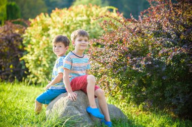 Bir kaya üzerinde güneşli parkta oturan iki çocuk akşam veya gün konusunda sizi uyarır. Sezon, çocuklar, yaşam tarzı kavramı