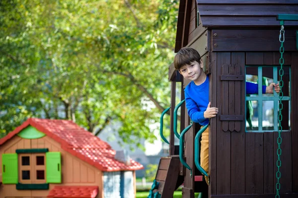 Niño escalando escalera en el tobogán en el patio de recreo. El niño tiene 5 7 años. Caucásica, casual vestida con jeans y jersey. Niños jugando al aire libre en verano. Concepto de infancia saludable —  Fotos de Stock
