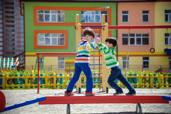 İki küçük okul çocuğu ve anaokulu çocuğu dışarıda oyun oynuyorlar. Çocuklar yaz güneşli bir günde açık hava aktiviteleri ile kütüğün üzerinde yarışacaklar.