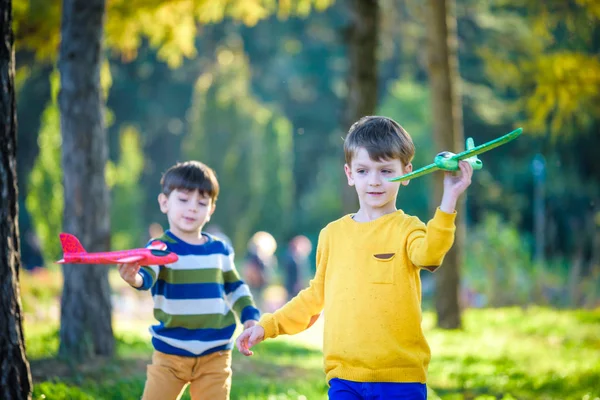 Happy two brother kids playing with toy airplane against blue summer sky background. Boys throw foam plane in the forest or park. Best childhood concept — Stock Photo, Image