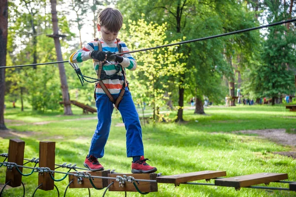 Fröhliches Kind spielt im Abenteuerpark, hält Seile und klettert — Stockfoto