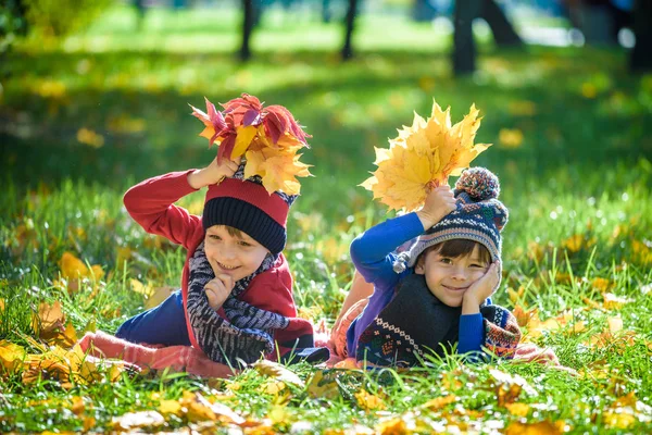 Menino bonito, criança pequena que coloca com um monte de folhas de outono amarelas no parque. Garoto se divertindo no dia de outubro quente ensolarado. Temporada, crianças, conceito de estilo de vida — Fotografia de Stock