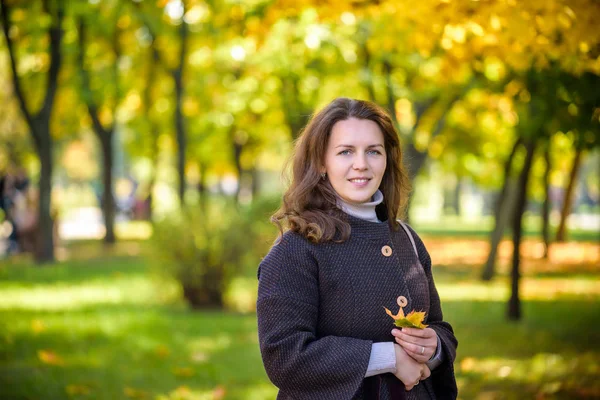 Young woman with autumn leaves in hand and fall yellow maple garden background — Stock Photo, Image