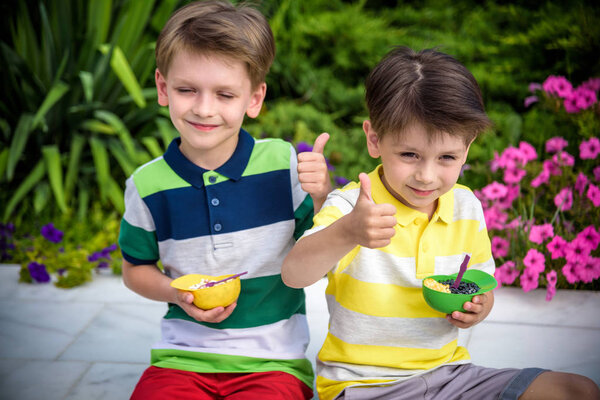 Tasty summer obsession concept. Happy young handsome hipster boys wearing sleeveless shirts with sharks, hugging, eating melting ice cream in waffle cone over pink colour background. Copy-space
