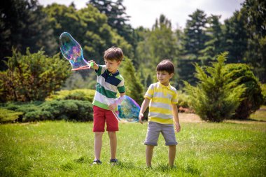 Heyecanlı bir çocuk baloncukların tadını çıkarırken çocuk sabun köpüğü üflüyor. Mutlu genç çocuk ve kardeşi parkta sabun köpüğü yapmayı seviyorlar. Mutlu çocukluk arkadaşlığı kavramı