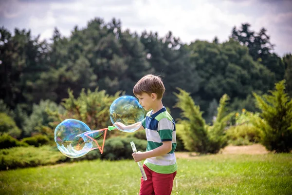 Kleiner Junge spielt mit seinem Seifenblasen-Spielzeug im Park. Kinderaktivität. Frühlingskonzept — Stockfoto