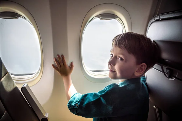 Хлопчик літає, дивлячись у вікно літака або отвір — стокове фото