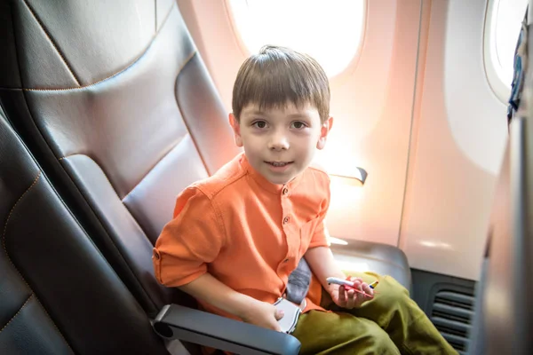 Дитина в літаку. Дитина в літаку сидить у віконному кріслі. Політ розваг для дітей. Подорожувати з маленькими дітьми. Діти літають і подорожують. Сімейні літні канікули. Маленький хлопчик з іграшкою в літаку — стокове фото