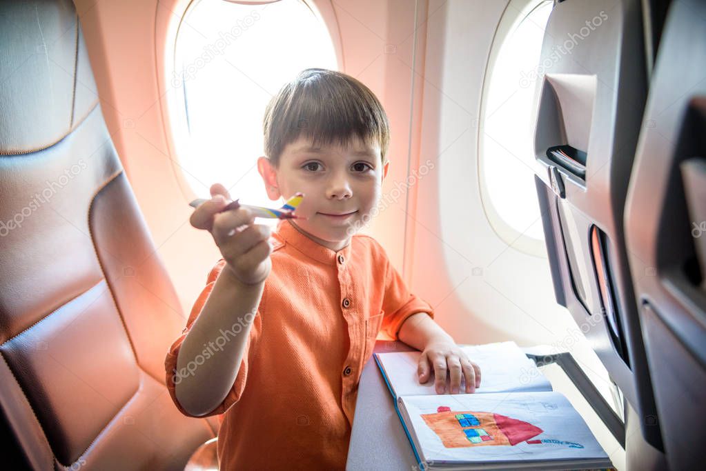 Charming kid traveling by an airplane. Joyful little boy sitting by aircraft window during the flight. Air travel with little kids