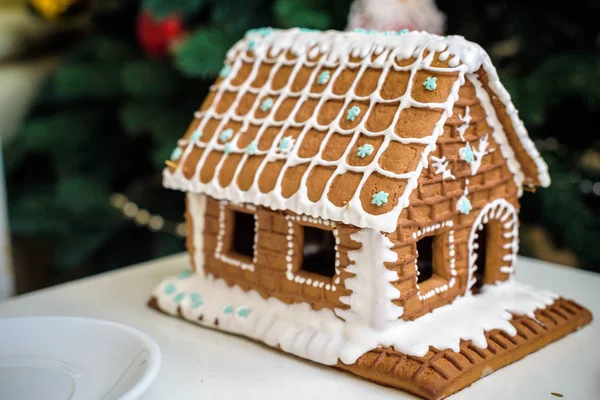 Hausgemachtes Lebkuchenhaus im Schnee. geschmückter Weihnachtsbaum im Hintergrund — Stockfoto