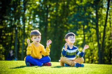 İki beyaz erkek kardeş taze yeşil çimlerin üzerinde oturup günlük giysiler içinde meditasyon yapıyorlar..