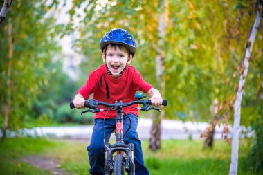 Başında koruyucu bir kask küçük bir beyaz Toddler çocuk bir çocuk bisiklet oturur. İki tekerlekli kırmızı bisikletli toddler ileriye bakıyor. Çocuğun yüzünde bir sly gülümseme