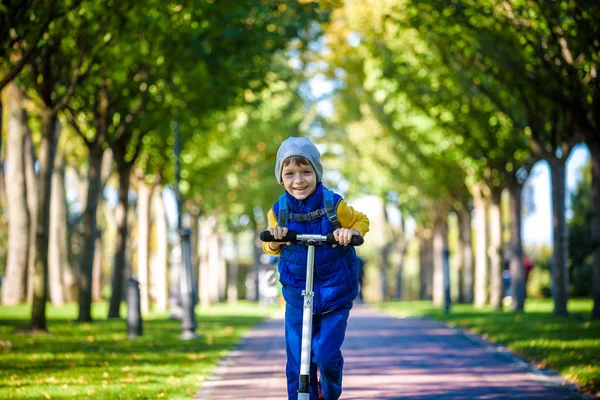 Un chico guapo montando un scooter en un parque de otoño —  Fotos de Stock