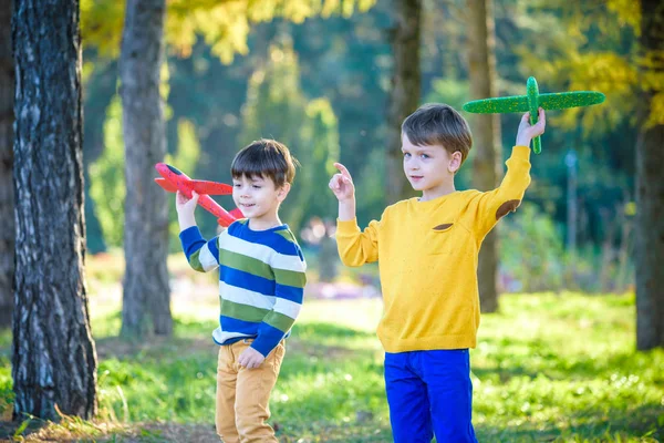 Mavi yaz gökyüzü arka planında oyuncak uçakla oynayan mutlu iki kardeş. Çocuklar ormana ya da parka köpük uçak fırlatırlar. En iyi çocukluk kavramı — Stok fotoğraf