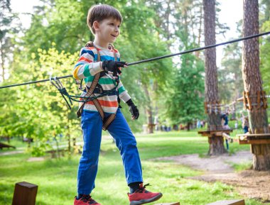 Mutlu çocuk macera parkında oynuyor, ip tutuyor ve tahta merdivenlere tırmanıyor..
