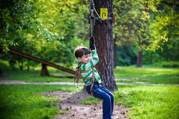 smiling boy rides a zip line. happy child on the zip line. The kid passes the rope obstacle course.