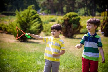 Heyecanlı bir çocuk baloncukların tadını çıkarırken çocuk sabun köpüğü üflüyor. Mutlu genç çocuk ve kardeşi parkta sabun köpüğü yapmayı seviyorlar. Mutlu çocukluk arkadaşlığı kavramı.