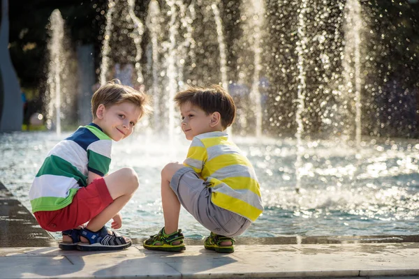 Tatlı çocuk ve abiler, bir jet fıskiyesinde su sıçratarak oynuyorlar, yaz mevsimi konsepti.