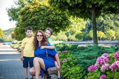 Genç bir kadın çocuklarıyla parkta oynarken eğleniyor. İlkokul çağındaki çocuklar. Aile pitoresk bitkilerle çevrili. Açık hava oyunları herkes için kullanışlı.
