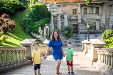 Genç bir kadın çocuklarıyla parkta oynarken eğleniyor. İlkokul çağındaki çocuklar. Aile pitoresk bitkilerle çevrili. Açık hava oyunları herkes için kullanışlı.