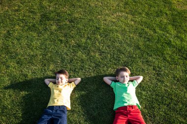 Parkta eğlenen iki kardeşin fotoğrafı, yeşil çimenlere uzanan iki neşeli çocuk, dışarıda oynayan küçük çocuk, en iyi arkadaşlar, mutlu aile, aşk ve mutluluk konsepti..