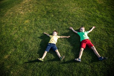Parkta eğlenen iki kardeşin fotoğrafı, yeşil çimenlere uzanan iki neşeli çocuk, dışarıda oynayan küçük çocuk, en iyi arkadaşlar, mutlu aile, aşk ve mutluluk konsepti..