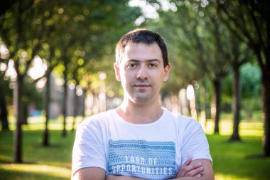 Açık havada beyaz gömlekli, doğa parkında gülümseyen güzel bir adamın portresini kapat. Moda modeli.