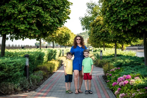 Genç bir kadın çocuklarıyla parkta oynarken eğleniyor. İlkokul çağındaki çocuklar. Aile pitoresk bitkilerle çevrili. Açık hava oyunları herkes için kullanışlı.